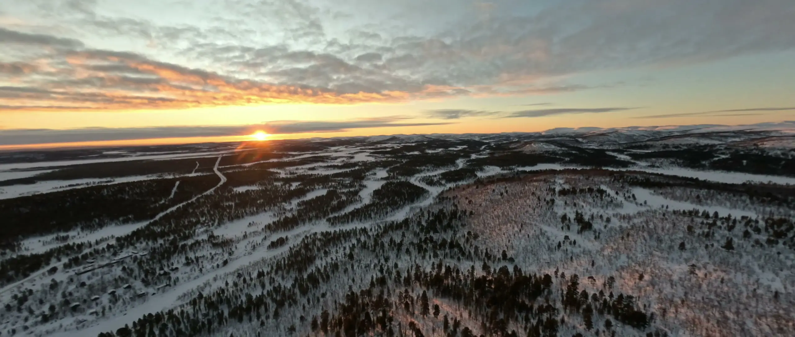 Aerial view of the fell country at sunset, with the river and the road winding through snowy forest