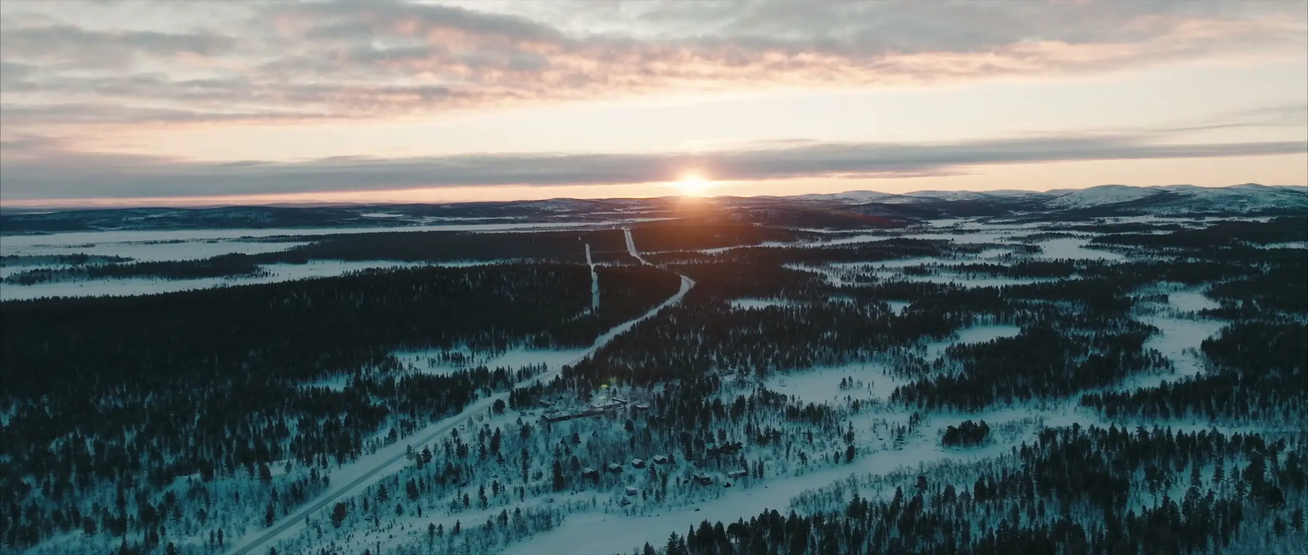 Aerial view of the snowy fell country at sunrise, with a road through the forest