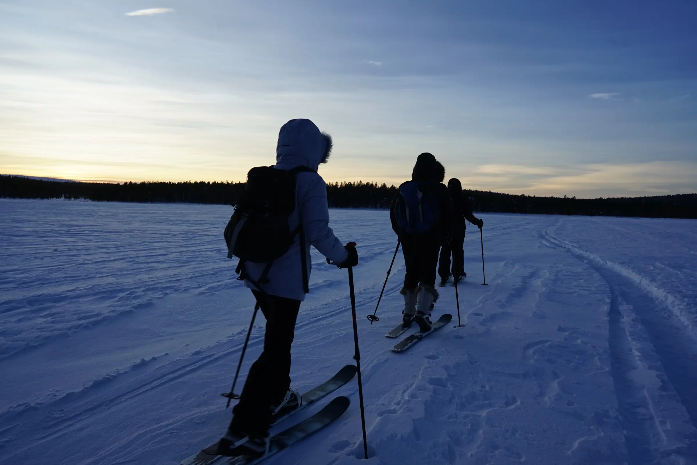 Four skiers cross a frozen lake at dusk