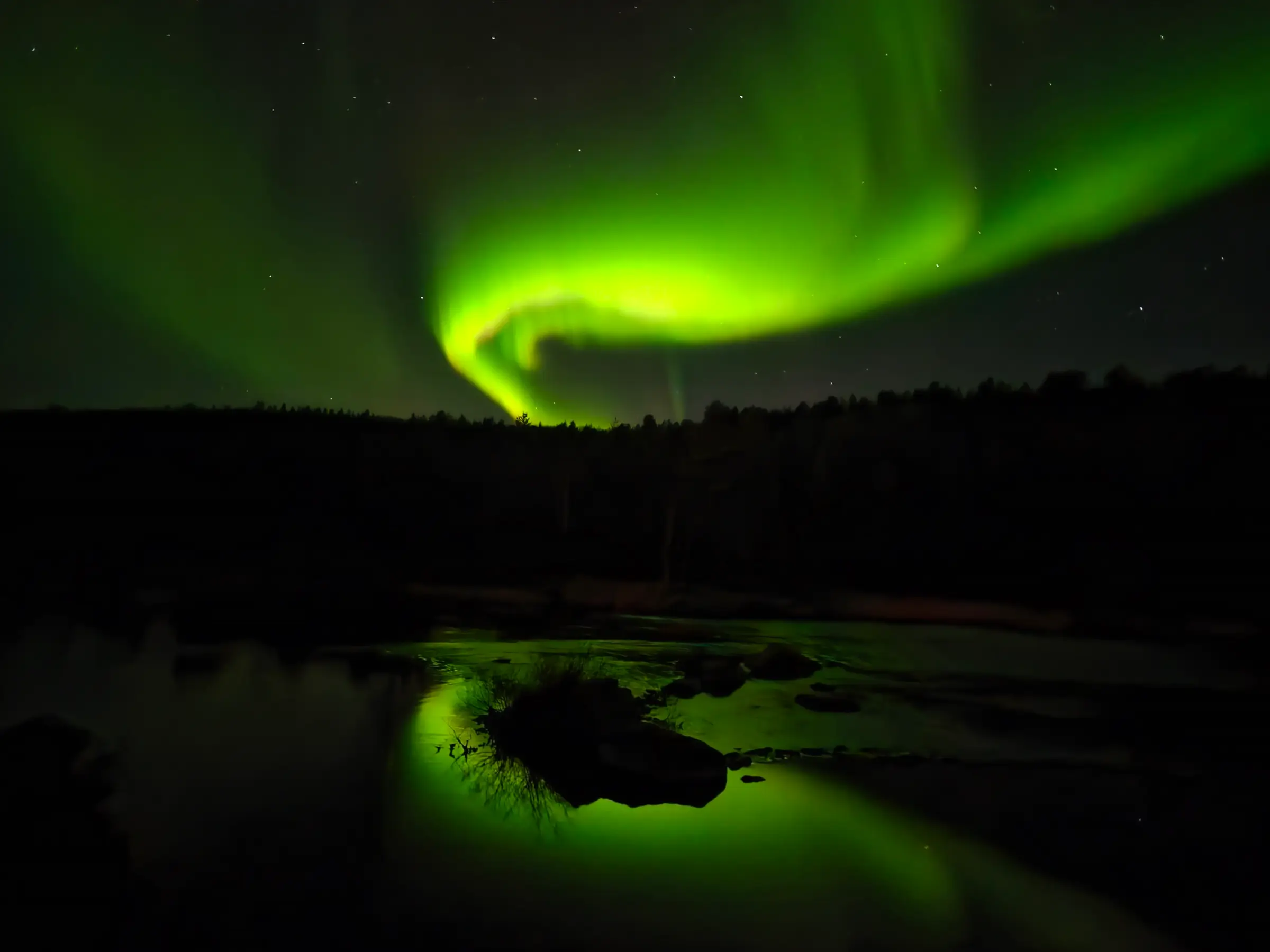 Green northern lights over the forest, reflected in the still river