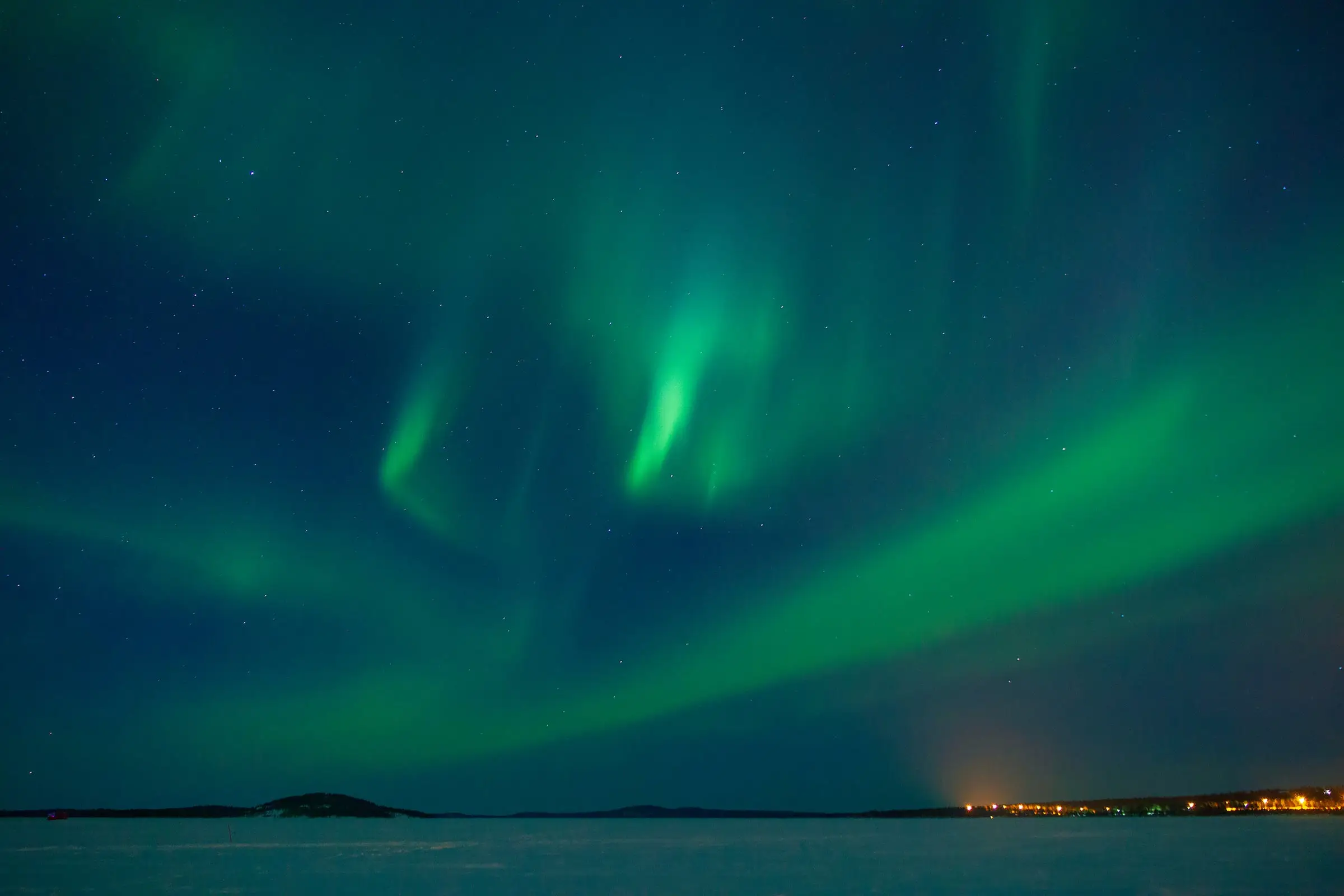 Green northern lights in soft bands above a frozen bay of Lake Inari