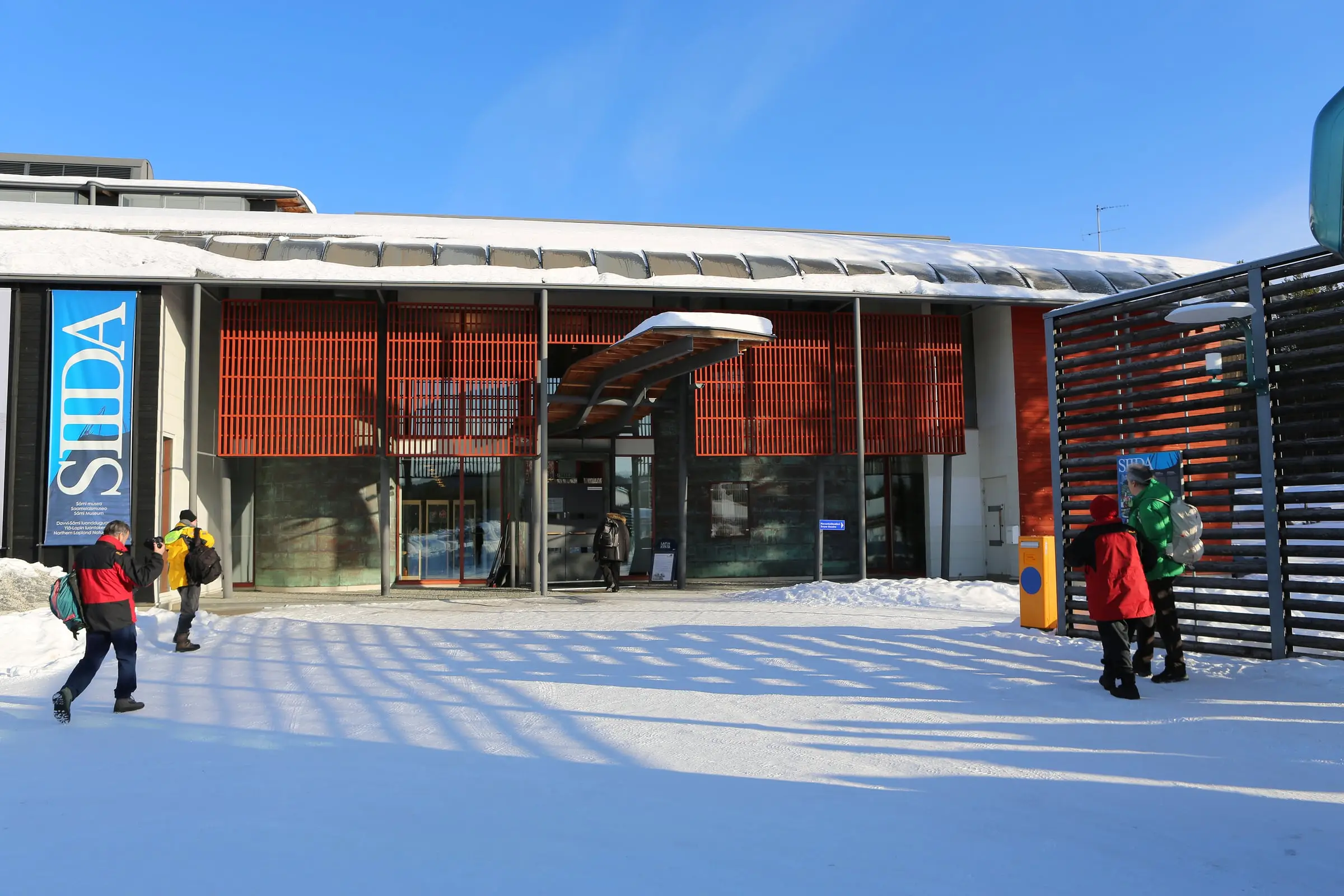 The entrance of the Siida museum in Inari on a sunny winter day, with visitors walking on the snow