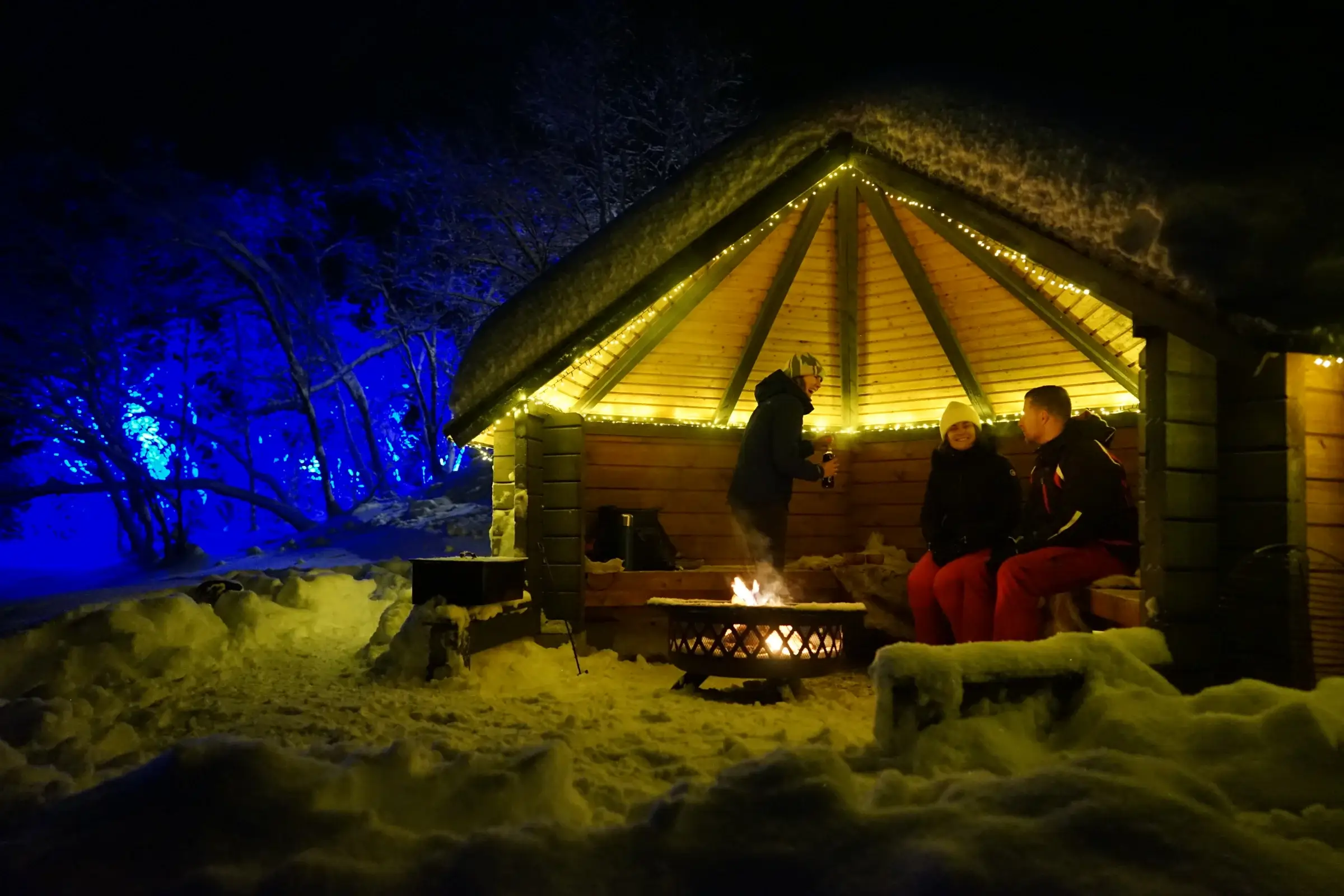 The kota, a round log hut with a snow-covered roof, among birches in the winter village