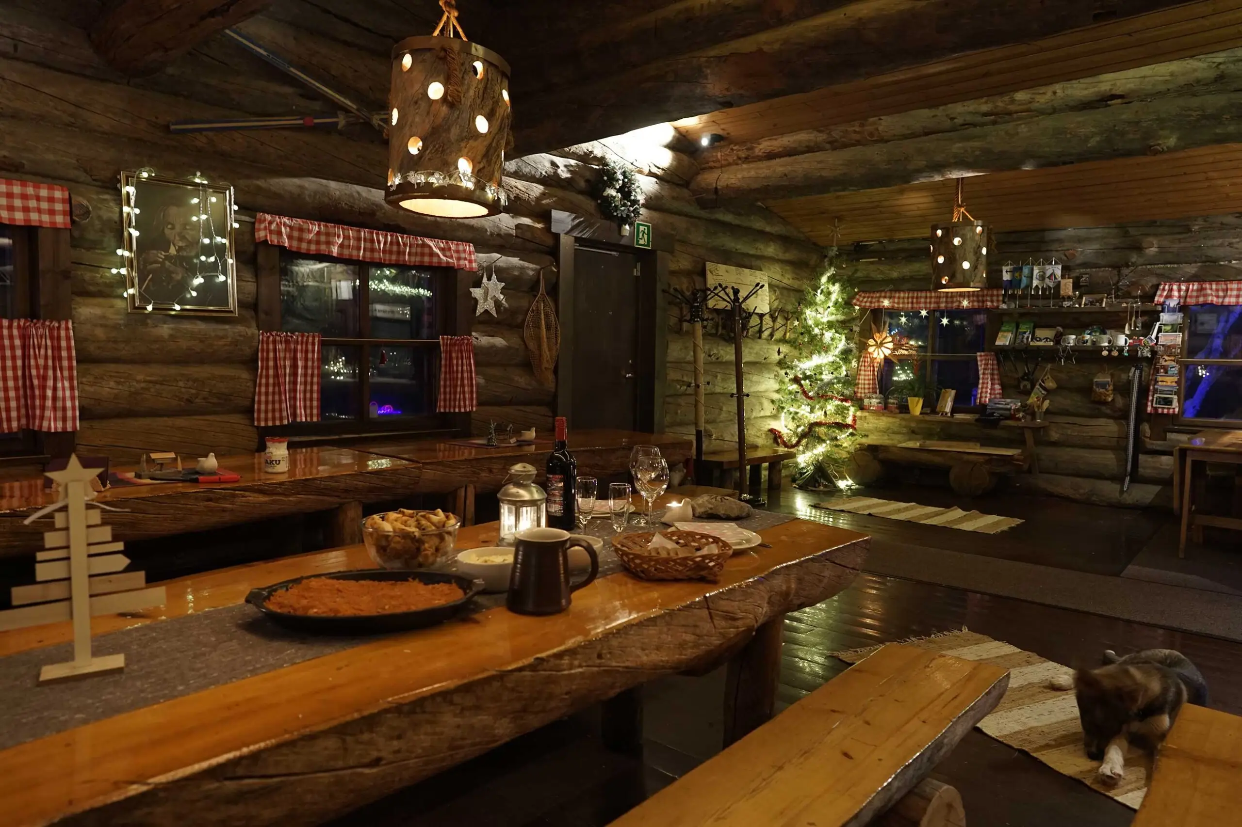 The log dining room set for dinner, with candles, a Christmas tree and a cat by the bench