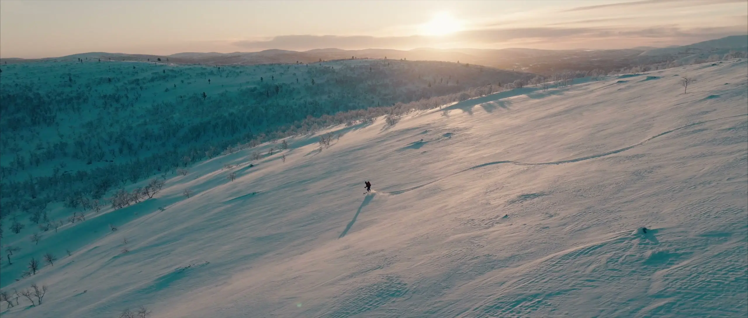 A lone skier crossing a wide snowy fell in the low winter sun